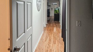 A hallway with a wooden floor, a white door with a keyhole, and a wall clock. - Escondido Urban Stay - Stylish 2BR Apartment (Escondido)