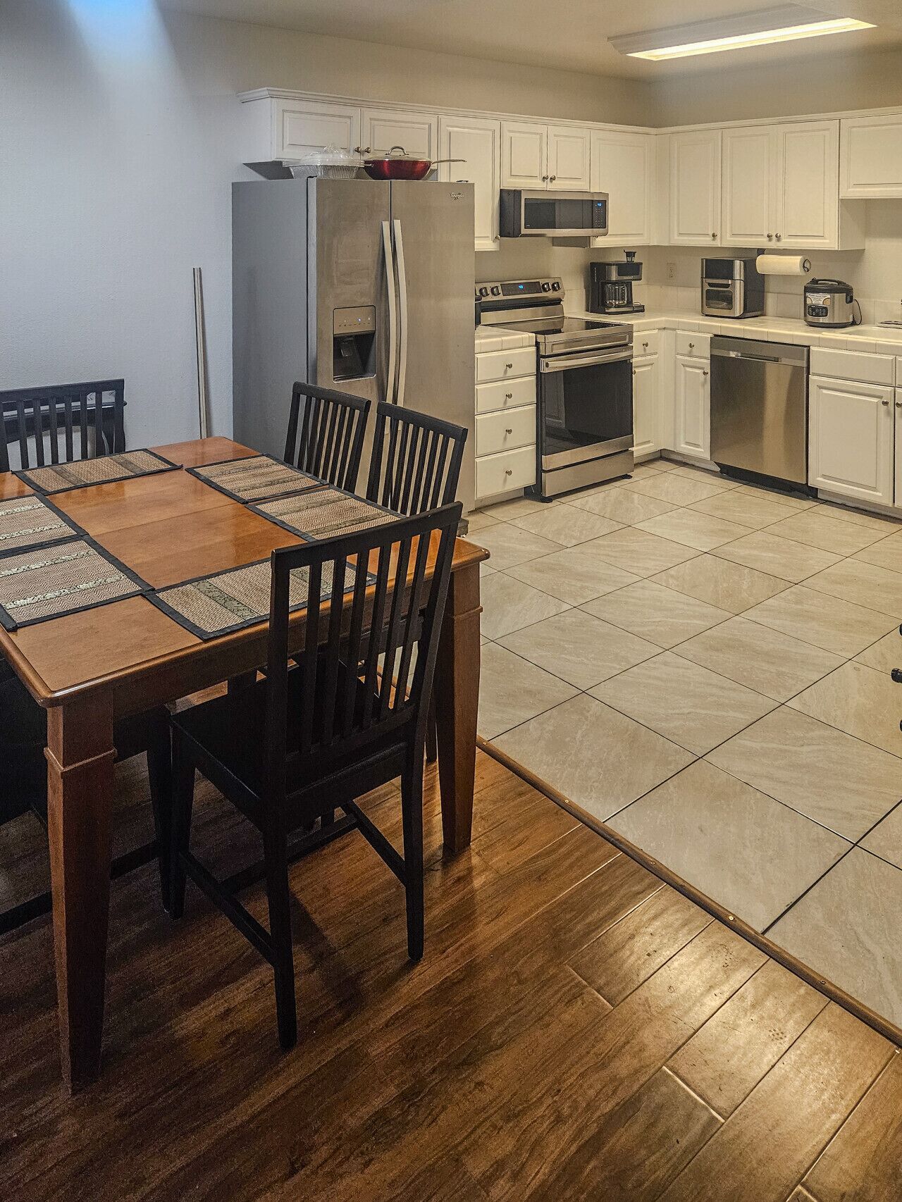Une cuisine moderne avec des armoires blanches, des appareils en acier inoxydable, une table à manger avec des chaises et un plancher en bois.