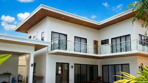 Una casa moderna de dos pisos con piscina, ventanas amplias y un balcón.