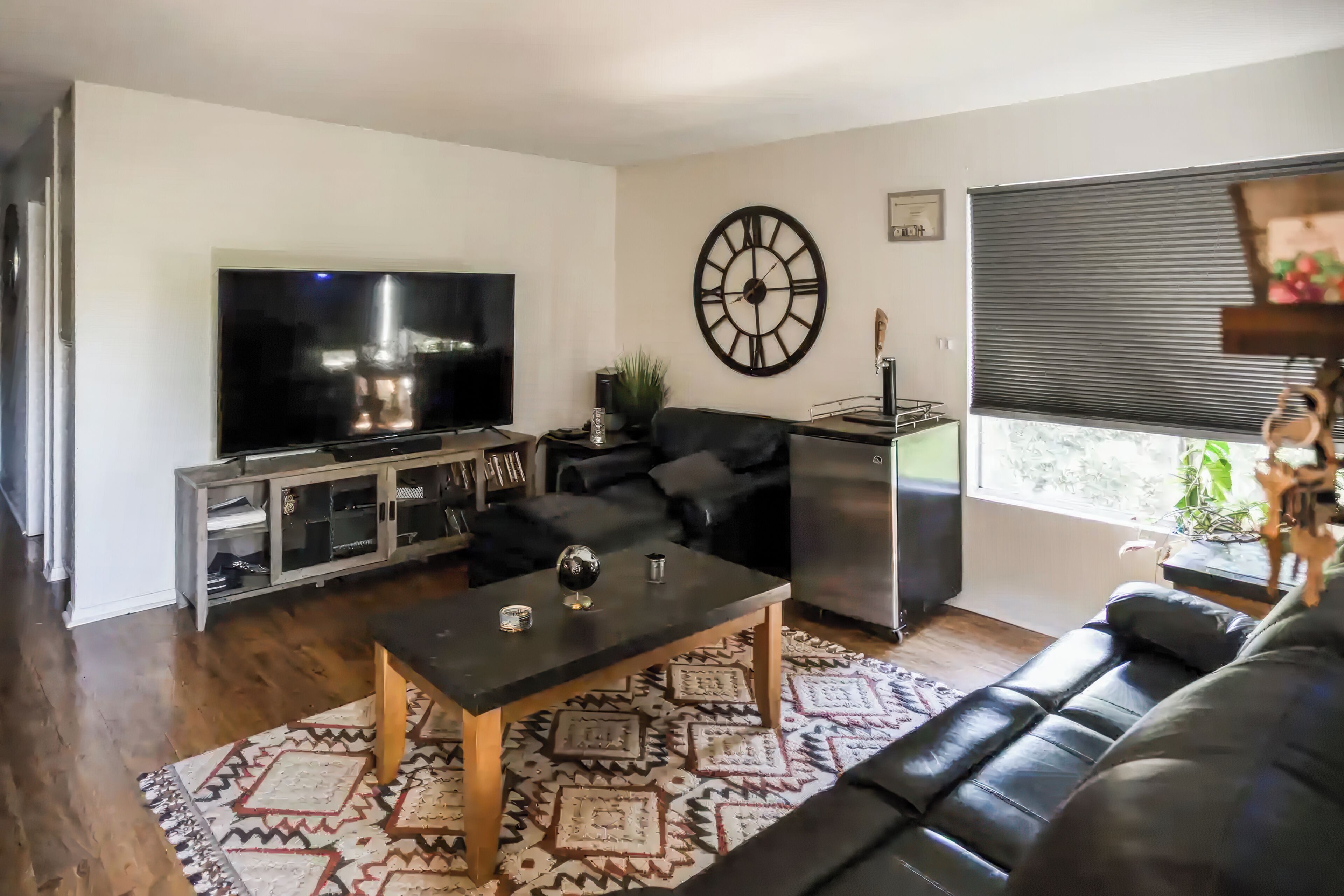 A living room with a flat-screen TV, a large wall clock, a sofa, a coffee table, and a patterned rug.