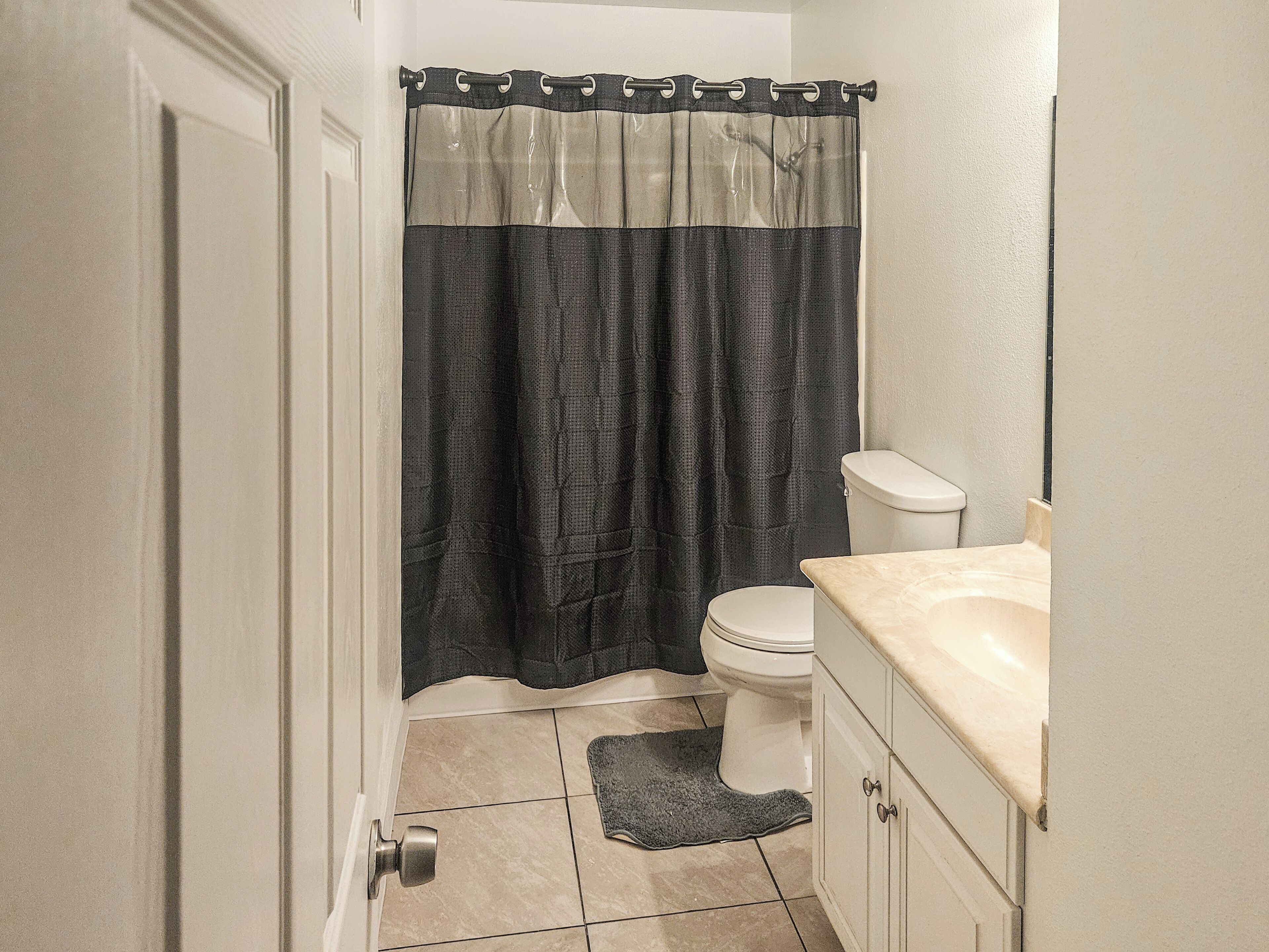 A bathroom with a toilet, a sink, a shower curtain, and a door.