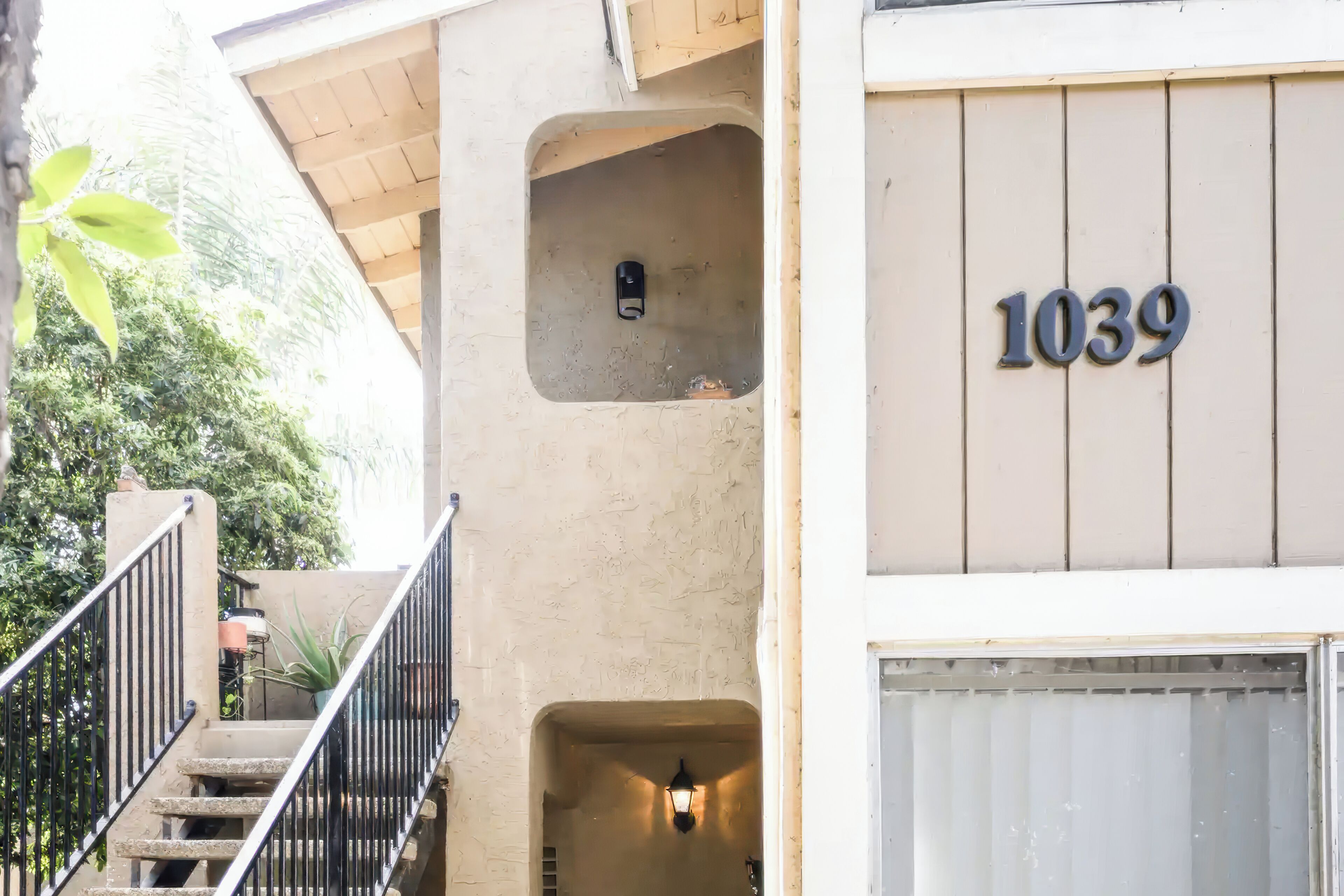 A building with a beige exterior, a staircase with black railings, a potted plant, and a number '1039' sign.