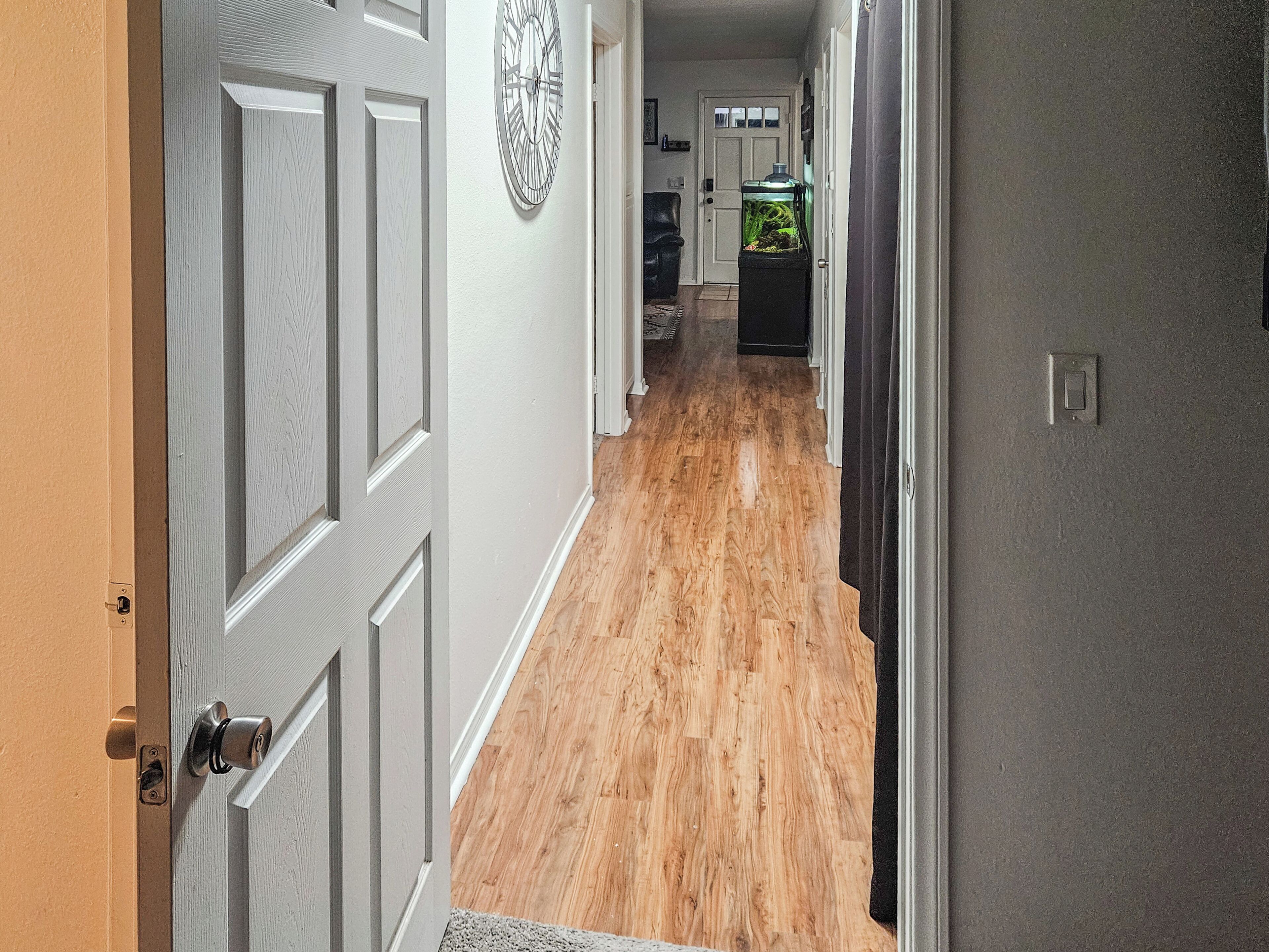 A hallway with a wooden floor, a door with a keyhole, and a wall clock.