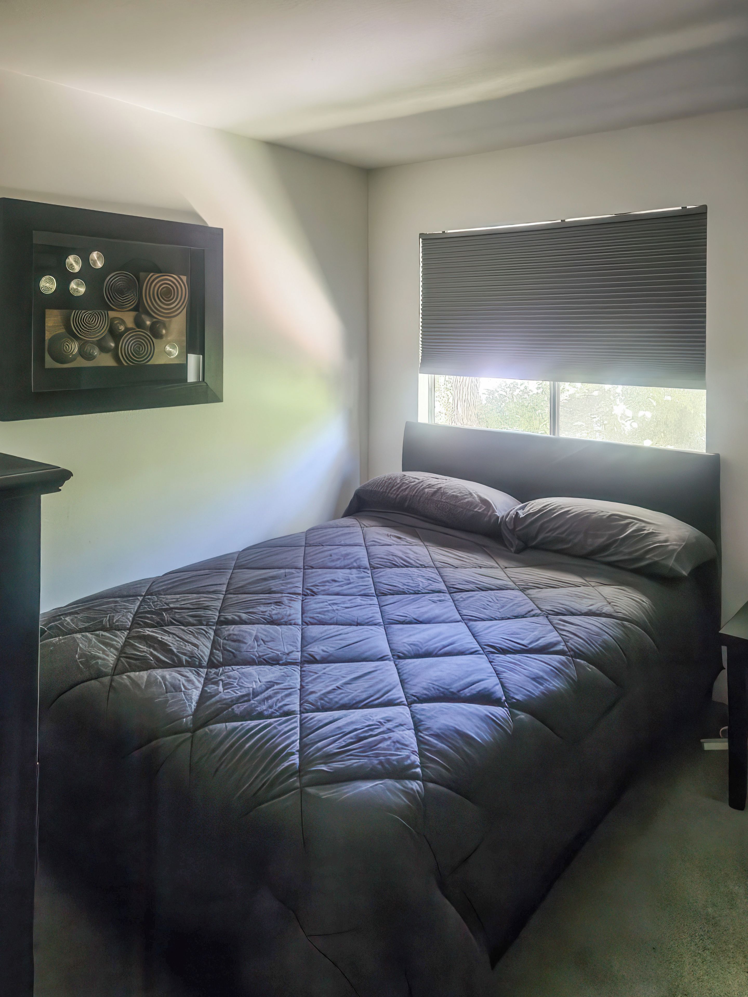 Une chambre à coucher avec un lit, une fenêtre avec des stores et une œuvre d’art accrochée au mur.