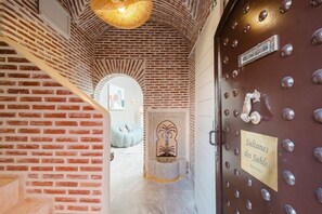 A hallway with a brick wall, a staircase, a door with a brass handle, and a sign reading 'Sultanes des Sables.' - Riad Sultanes-Peaceful haven with private Jacuzzi (Marrakech)