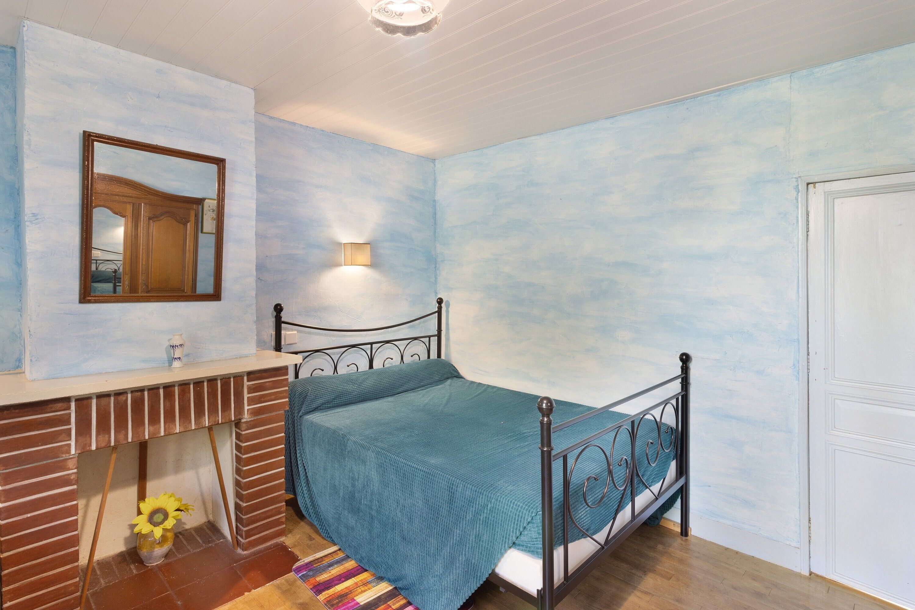 Une chambre à coucher avec un lit, un miroir, une lampe fixée au mur et une porte.