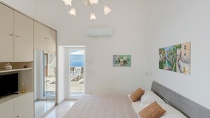 Quarto com cama, televisão, guarda-roupa e porta para uma varanda.