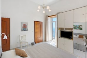 Un dormitorio con cama, una silla, televisor, armario y puerta.