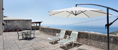 Un patio con tavolo e sedie, un ombrellone bianco e vista sul mare.