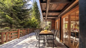 Eine Holzterrasse mit Tisch und Stühlen, umgeben von einem Holzzaun und Bäumen.