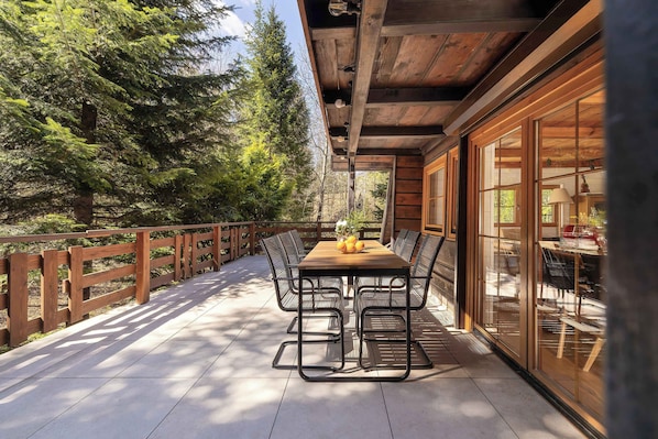 A wooden deck with a table and chairs, surrounded by a wooden fence and trees.