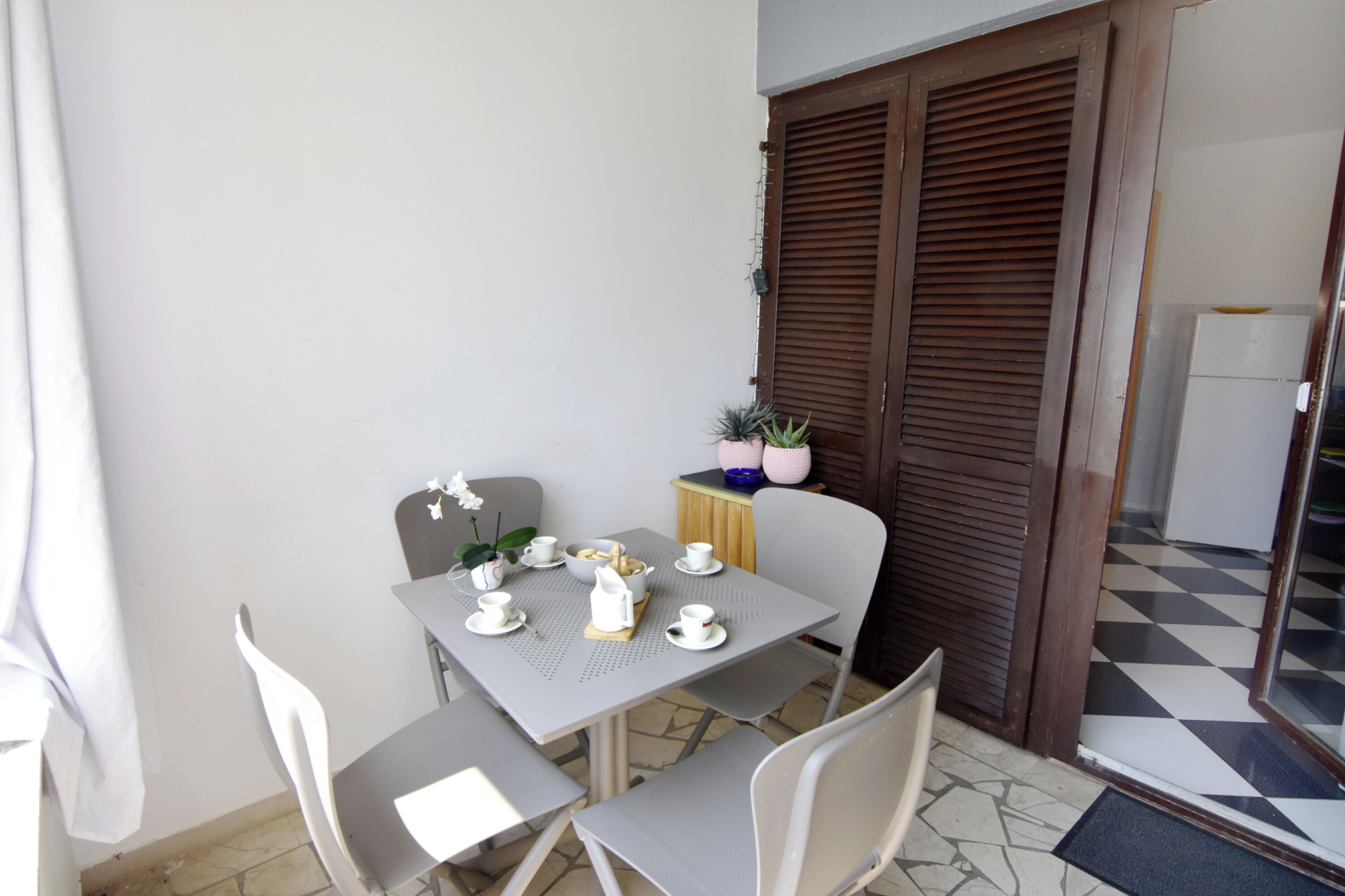 A small dining area with a table set for two, a chair, a potted plant, and a wooden door.
