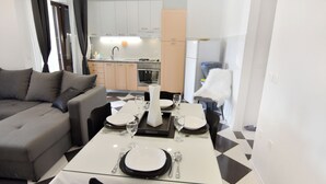 A modern living room with a dining area set for four, a kitchen in the background, and a white chair. - Stylish Renovated Vacation Flat With Terrace (Umag)