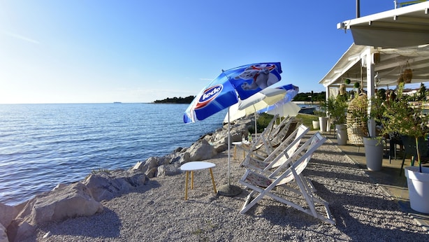A beachside area with pebbled ground, lounge chairs, and umbrellas. - Stylish Renovated Vacation Flat With Terrace (Umag)