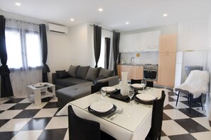 Ein modernes Wohnzimmer mit einer Couch, einem Esstisch für zwei Personen und einer Küche im Hintergrund.