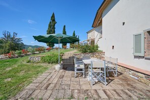 Eine Terrasse mit Tisch und Stühlen, einem grünen Sonnenschirm und einer Steinmauer.
