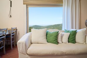 Una habitación con sofá, una mesa de comedor con sillas y una ventana con vistas a colinas verdes.
