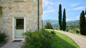 A stone building with a door, a gravel path, and a view of hills and trees. - Apartment 'Agriturismo Il Ghiaccio - Mirto' with Sea View, Wi-Fi and Air Conditioning (Suvereto)