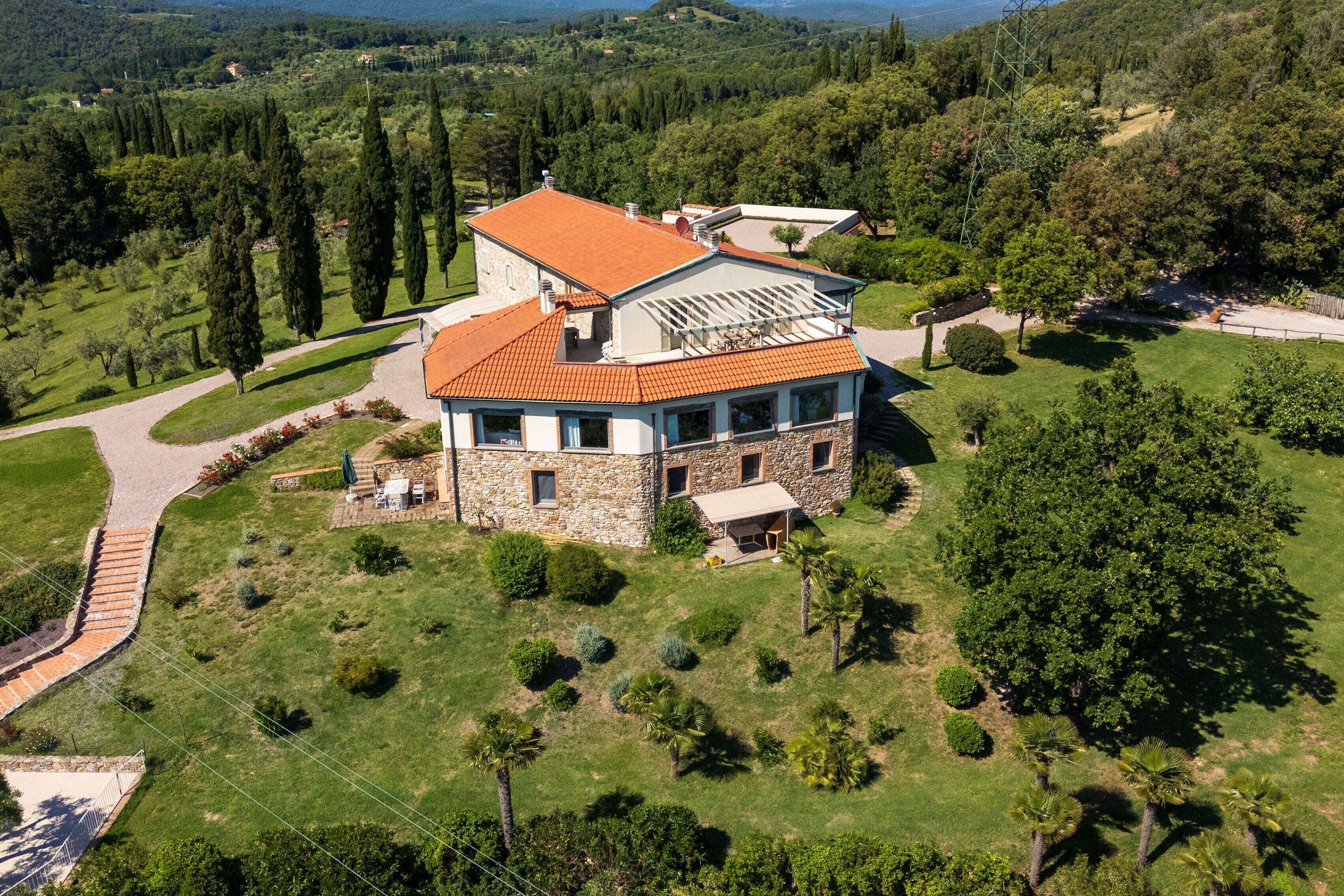 Une maison en pierre avec un toit rouge, entourée d’une végétation luxuriante et d’arbres.