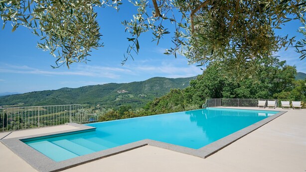 Ein rechteckiger Swimmingpool mit klarem, blauem Wasser, umgeben von einer Betonplattform und einem Metallzaun.