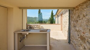 Eine kleine Küchenzeile mit Spüle und Fenster mit Blick auf ein Steinhaus und Grünflächen.