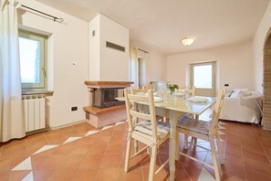 A dining area with a table, chairs, a fireplace, and a bed in a room with tiled flooring and white walls. - Apartment 'Agriturismo Il Ghiaccio - Quercia' with Shared Pool, Wi-Fi and Air Conditioning (Suvereto)