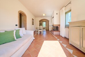 Ein Zimmer mit einer weißen Couch, einem Esstisch mit Stühlen, einem Kamin und einem gefliesten Boden.