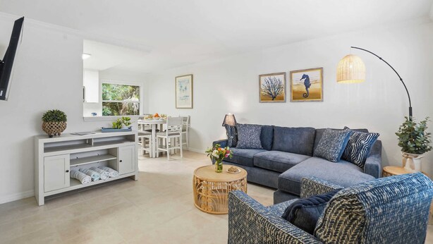 A modern living room with a grey sofa, a round coffee table, a white entertainment unit, and a dining area with a white table and chairs. - Under 1 Mile to Siesta Key Beach | Beach Gear Included | Pool | Sleeps 4 (Sarasota)