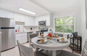 A modern kitchen with white cabinets, a stainless steel refrigerator, a microwave, and a dining table set with plates, glasses, and food. - Under 1 Mile to Siesta Key Beach | Beach Gear Included | Pool | Sleeps 4 (Sarasota)