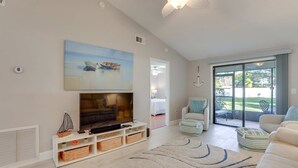Sala de estar con televisor, sofá y vistas al exterior.