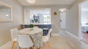 Una cocina moderna con gabinetes blancos, una mesa de comedor con mantel estampado y una lámpara colgante.