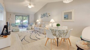 Una sala moderna con sofá, mesa de comedor y sillas, ventilador de techo y vista a través de una puerta de vidrio.