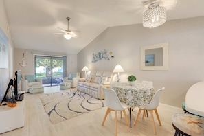 Ein modernes Wohnzimmer mit einer Couch, einem Esstisch, Stühlen, einem Deckenventilator und Blick durch eine Glastür.