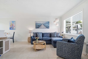 A living room with a sofa, armchair, coffee table, and artwork on the wall. - Flamingo-Themed Condo | 1 Mile to Siesta Key | Beach Gear Included | Pool (Sarasota)