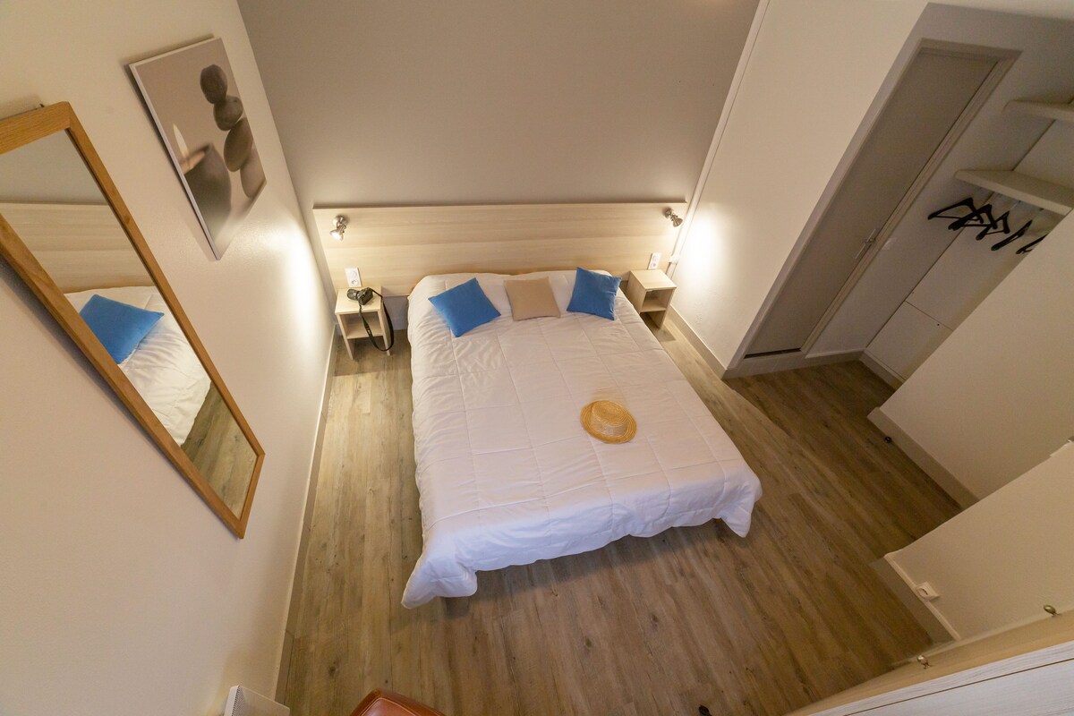 A hotel room with a large bed, a bedside table, a nightstand, a mirror, and a wardrobe.