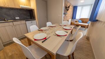 A dining area with a wooden table set for six, white chairs, and a kitchen in the background.
