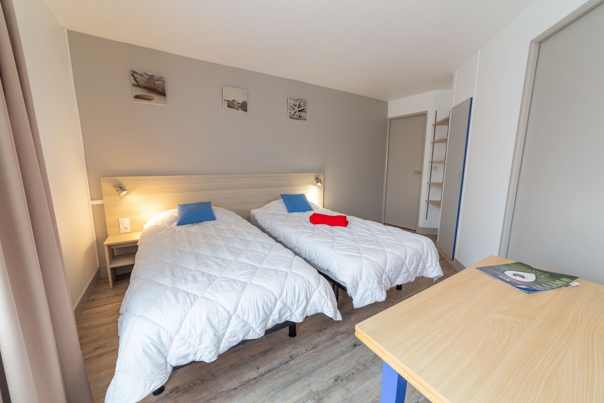 A hotel room with two beds, a wooden floor, a desk, and a door.