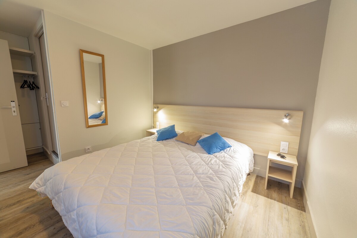 A bedroom with a large bed, two bedside tables, a nightstand, a mirror, and a wardrobe.