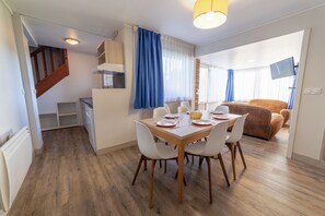 A modern kitchen with white cabinets, a dining area with a wooden table and white chairs, and a living area with a brown sofa.