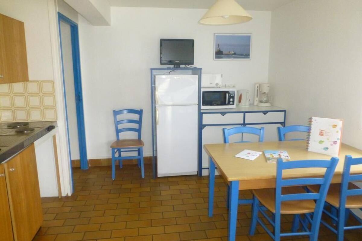 Cocina compacta con refrigerador, microondas y cafetera. Hay una mesa de comedor con sillas y una lámpara colgante.
