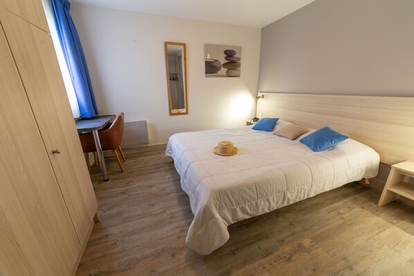 A bedroom with a bed, bedside table, lamp, and a desk with a chair.