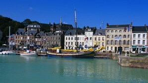 Ein Hafen mit einem großen Segelboot, Gebäuden mit Flaggen und einem strahlend blauen Himmel.