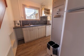 A compact kitchen with a window, a built-in oven, and a trash bin.