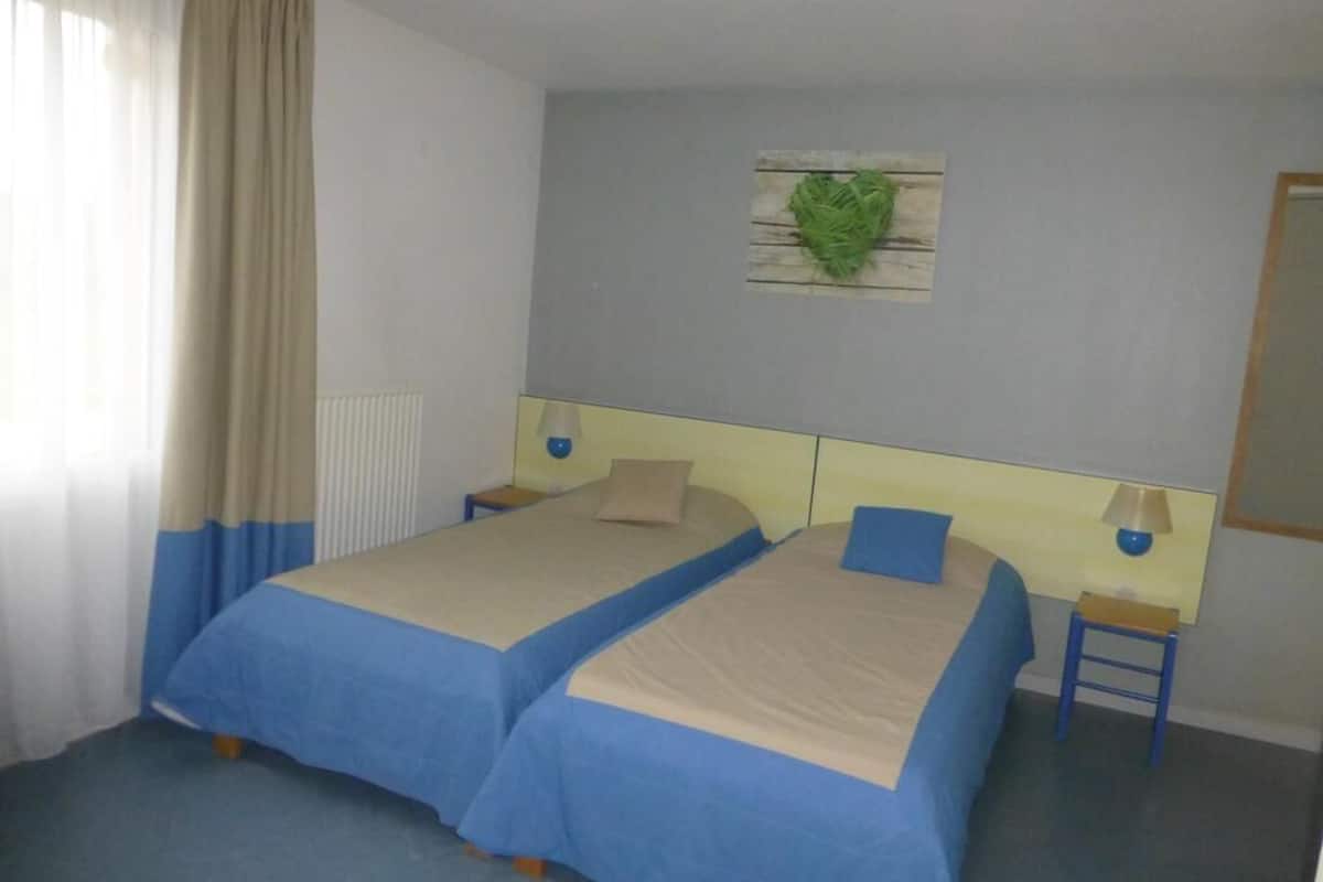 Una habitación de hotel con dos camas, una mesita, una lámpara y un adorno en la pared.