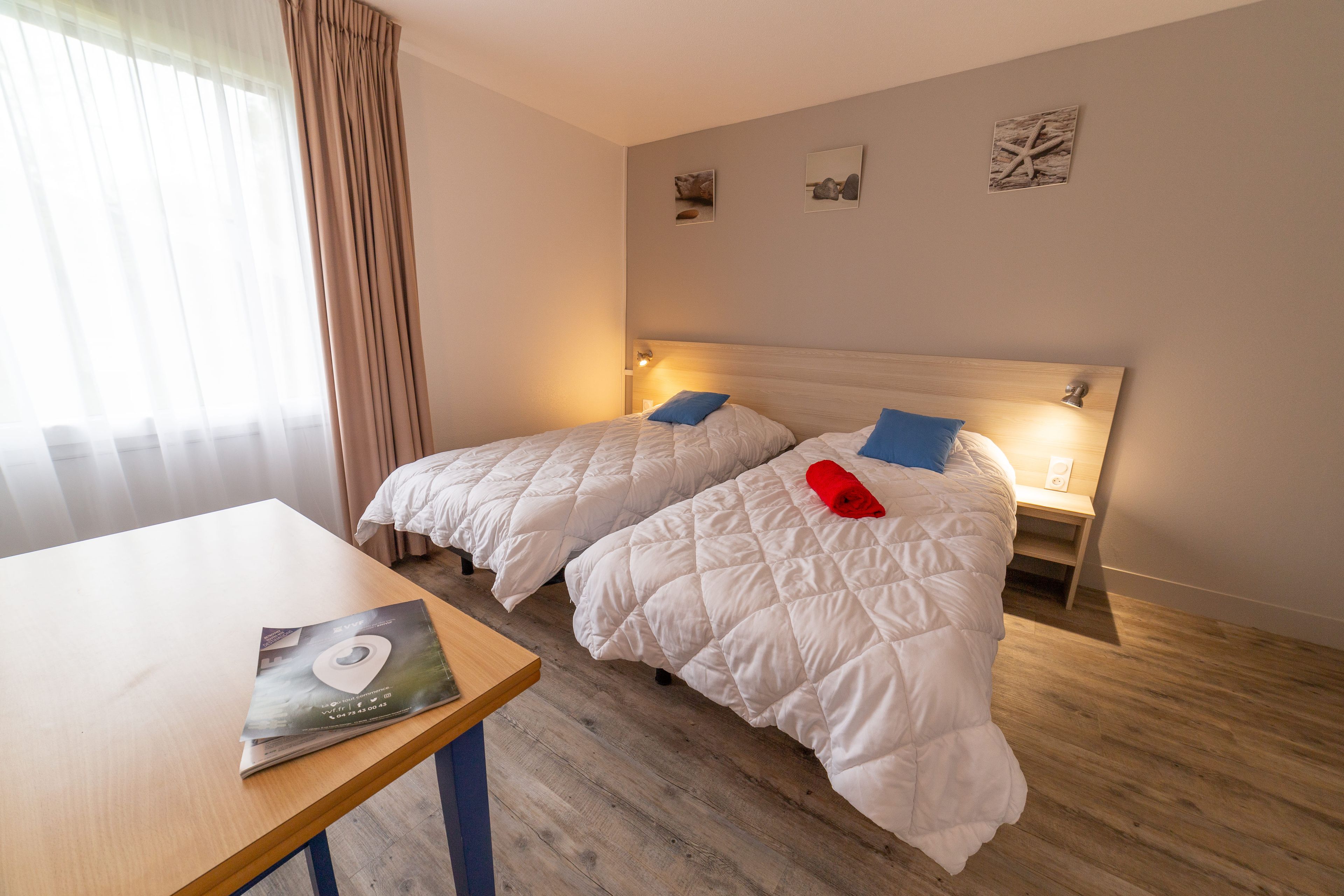 A hotel room with two beds, a wooden table, and a window with curtains.
