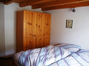 A bedroom with a wooden wardrobe, a bed with striped bedding, and a small framed picture on the wall. - Plaun Pazzola mit Garage Bösch, (Sedrun/Rueras), 684.01 by Interhome (Rueras Dieni)