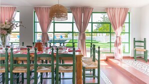 A dining area with a table set for four, green chairs, and large windows with curtains.