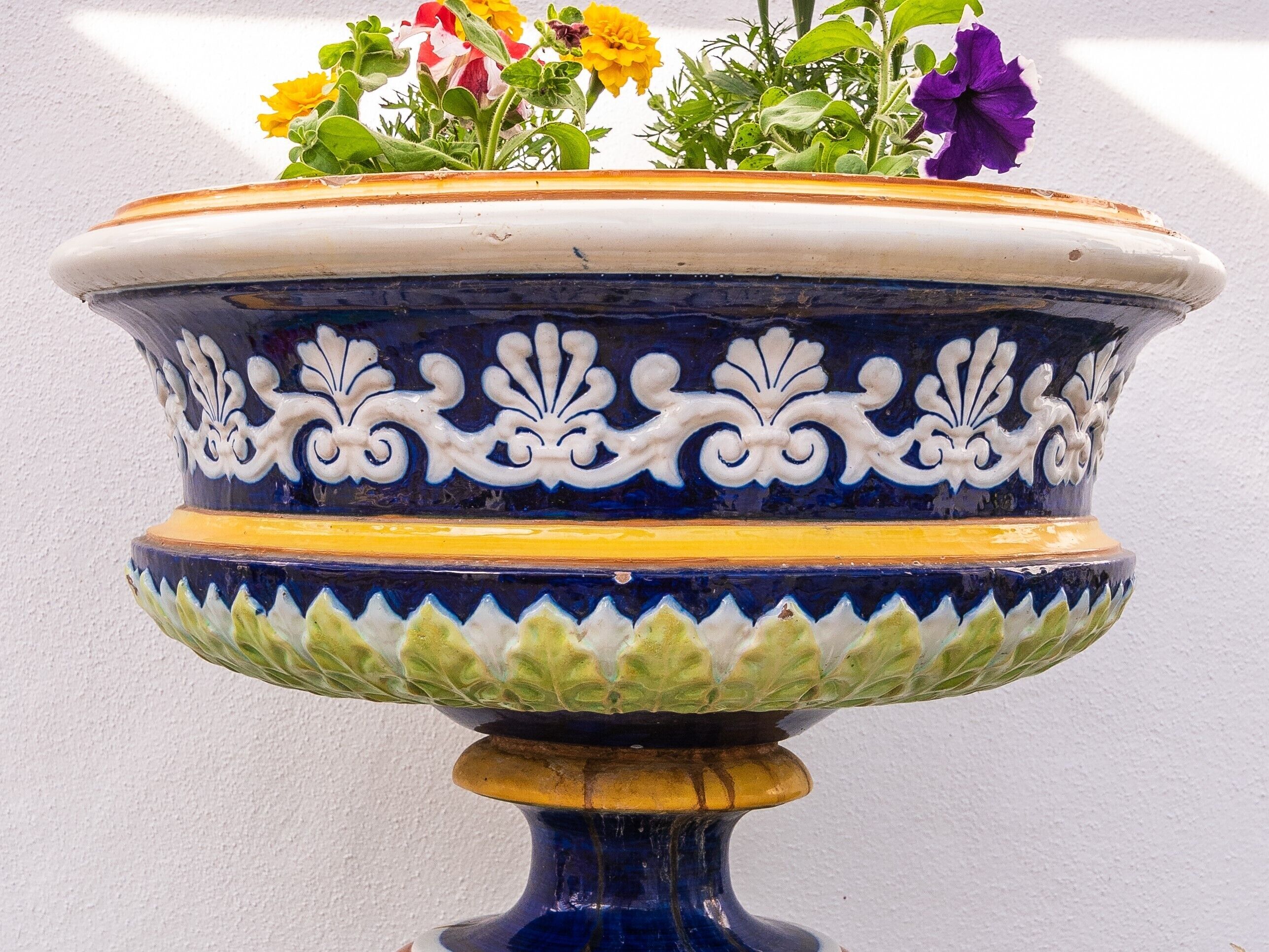 Una maceta de cerámica decorativa con diseños intrincados y un borde ancho, que contiene flores.