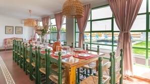 A dining area with a wooden table set for four, green chairs, and a view of a pool through large windows.