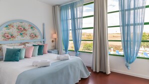 A bedroom with a bed, pillows, a nightstand, a lamp, and a view through large windows.